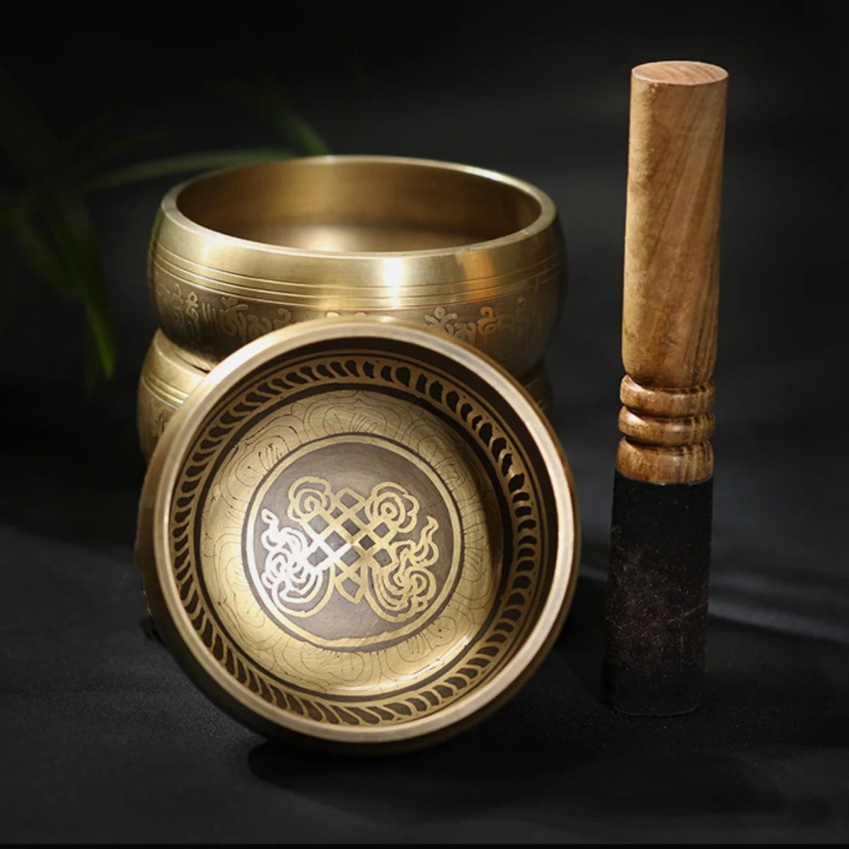 Image of a handcrafted CalmEcho Bowl Tibetan singing bowl, made in Nepal. The bowl is golden with an engraved traditional internal design, accompanied by a wooden striker with a padded end and a decorative blue and gold cushion. The set is used for meditation, yoga, and mindfulness practices, emitting relaxing and resonant sounds.