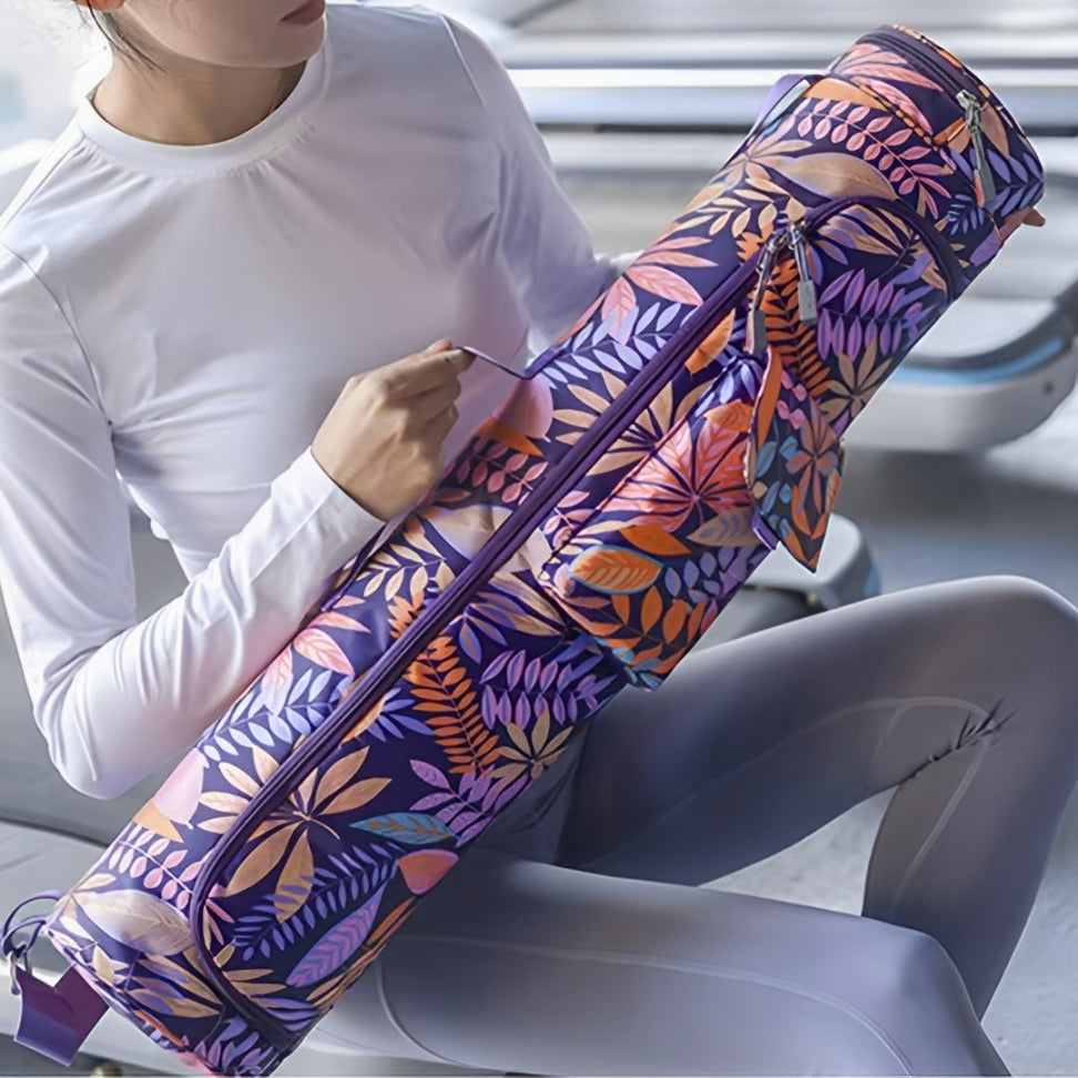 A yoga practitioner in a white long-sleeve top and gray leggings holds the FlexiMat Yoga Bag in the Tropical Flow design, showcasing its vibrant leaf-patterned print. The spacious, water-resistant bag securely holds a yoga mat and features multiple zippered compartments for storing essentials like towels, keys, and a phone. Designed with a comfortable adjustable shoulder strap, this lightweight and durable carrier is ideal for yoga classes, Pilates, or gym workouts.