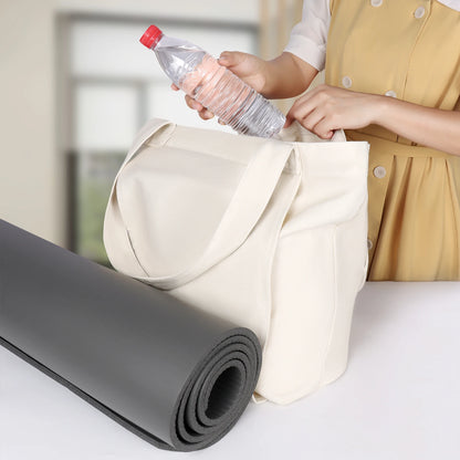 Image of the Essence Yoga Tote, a white, washable canvas bag designed for carrying yoga mats and workout essentials. The tote features a sleek and spacious design with adjustable straps for easy carrying. Shown with a rolled yoga mat secured in its front pocket, the tote is lightweight, foldable, and perfect for yogis on the go.