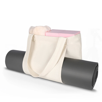 Image of the Essence Yoga Tote, a white, washable canvas bag designed for carrying yoga mats and workout essentials. The tote features a sleek and spacious design with adjustable straps for easy carrying. Shown with a rolled yoga mat secured in its front pocket, the tote is lightweight, foldable, and perfect for yogis on the go.