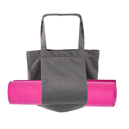 Image of the Essence Yoga Tote, a gray, washable canvas bag designed for carrying yoga mats and workout essentials. The tote features a sleek and spacious design with adjustable straps for easy carrying. Shown with a rolled yoga mat secured in its front pocket, the tote is lightweight, foldable, and perfect for yogis on the go.